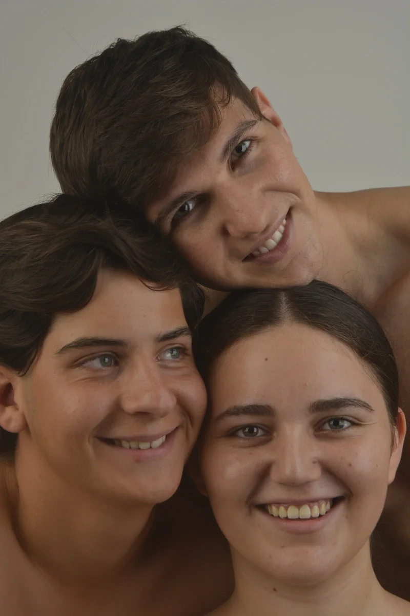 Tres modelos sonrientes con los rostros juntos sobre fondo gris