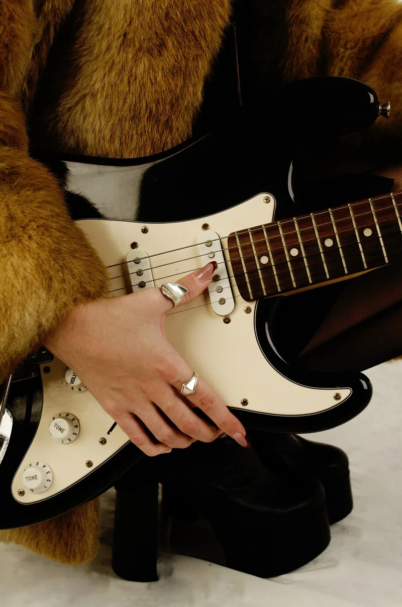 Detalle de manos con anillos sobre una guitarra eléctrica y botas de plataforma