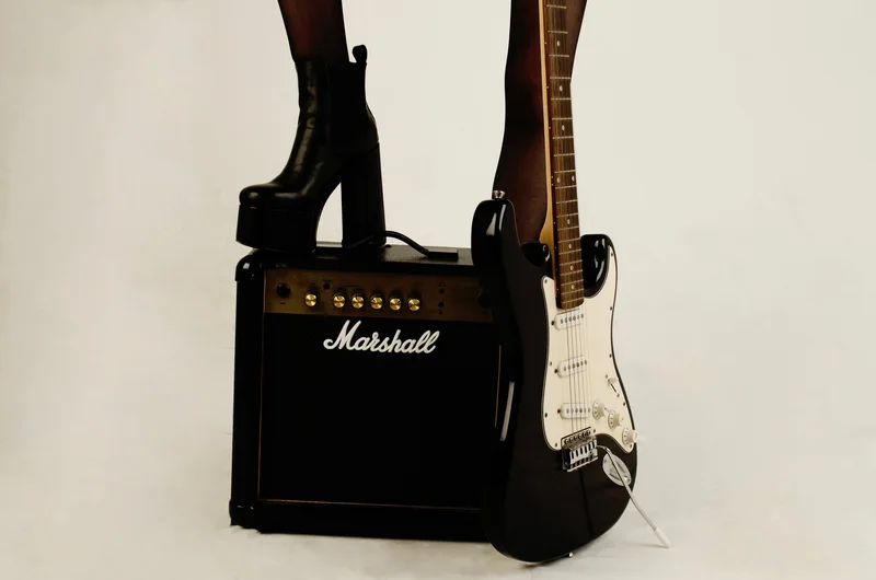 Piernas con medias y botas de plataforma junto a un amplificador Marshall y una guitarra