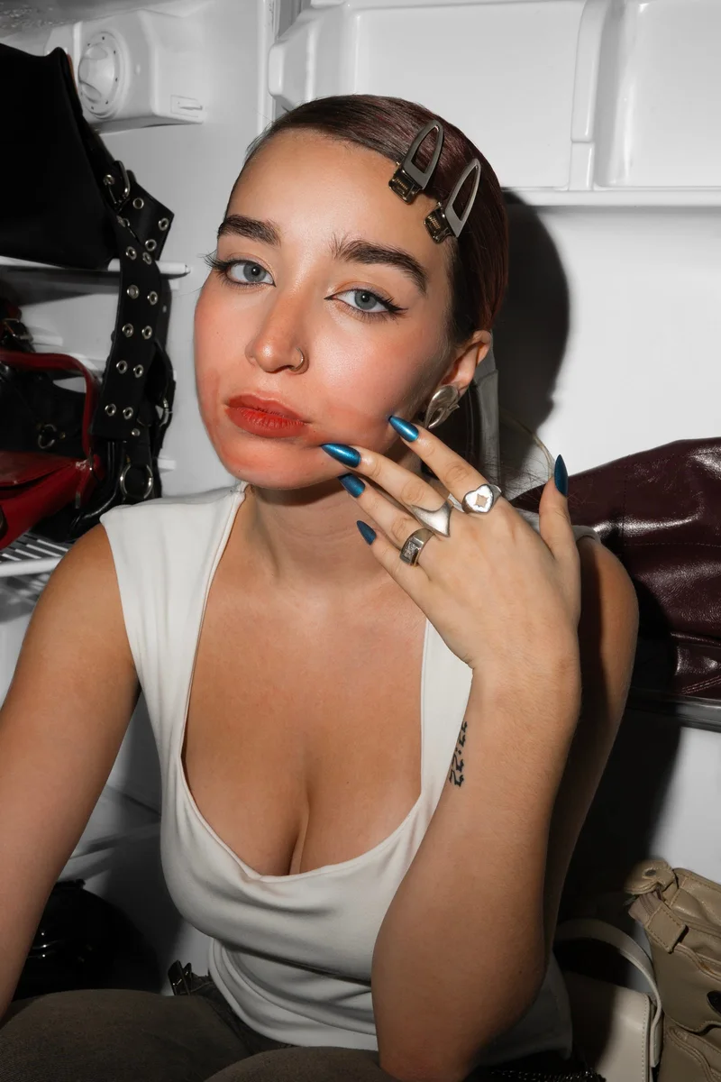 Modelo con uñas azules y anillos se toca los labios dentro de una heladera