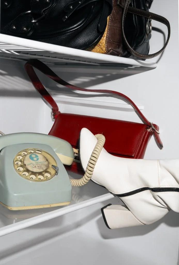 Estante de heladera con carteras, un teléfono antiguo y botas blancas