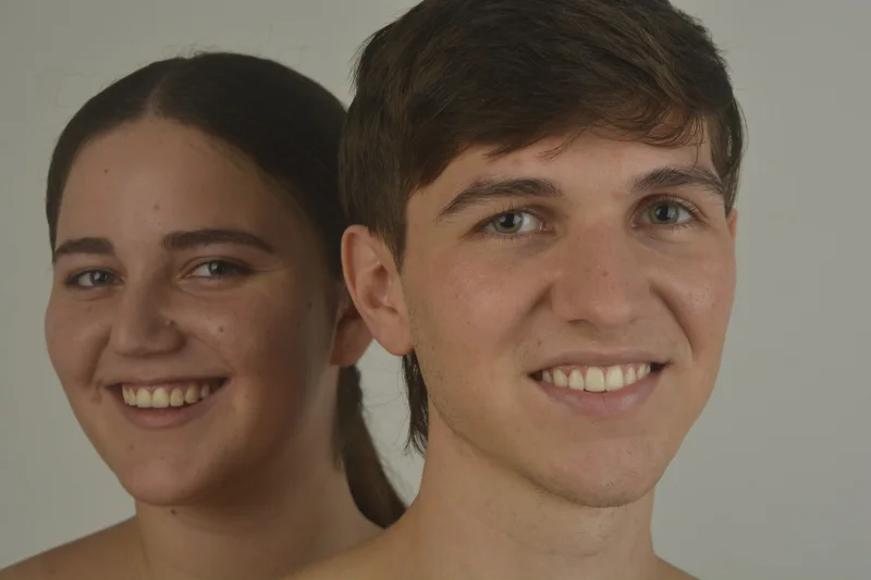 Dos modelos sonríen mejilla con mejilla sobre fondo gris